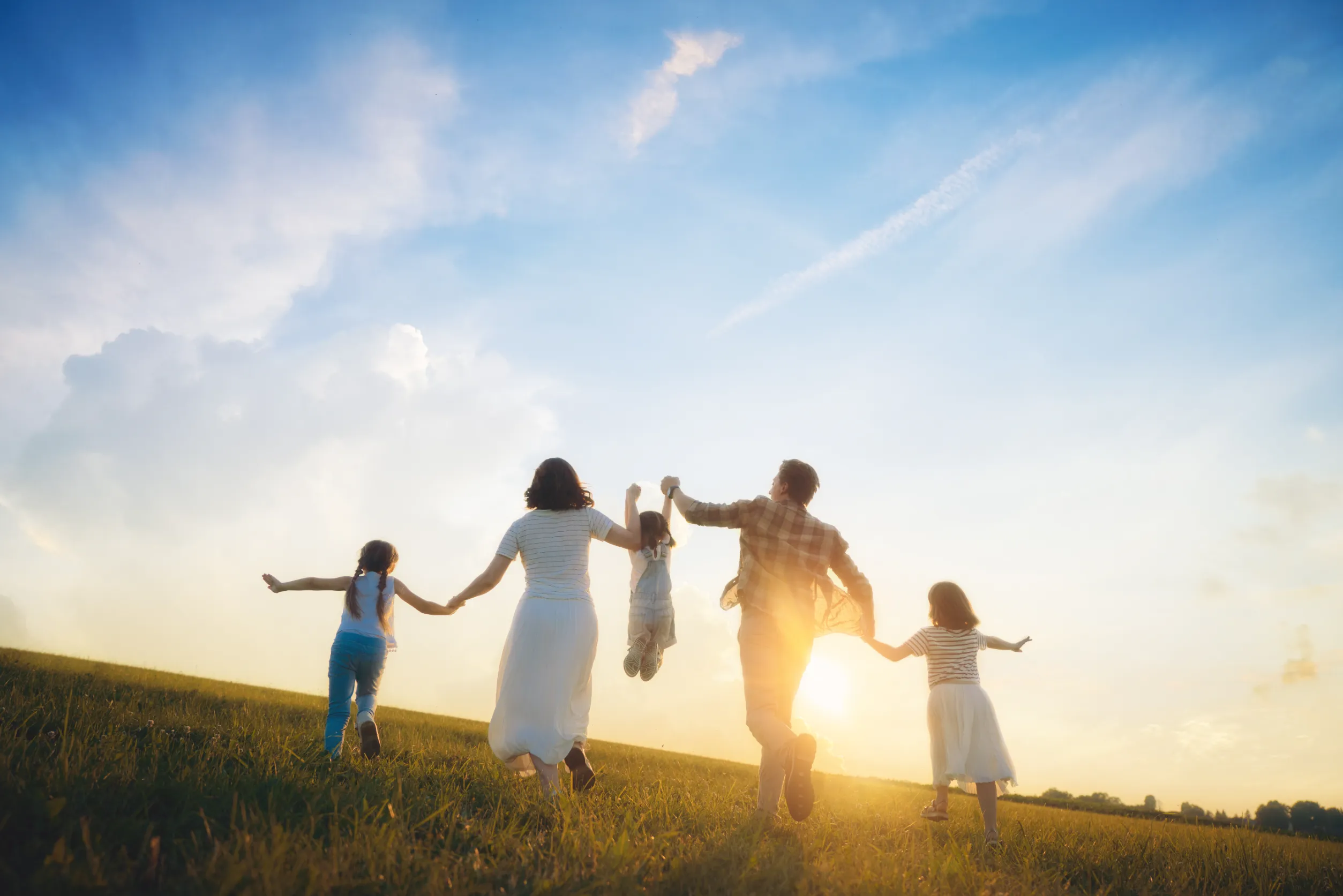 Happy family playing in the meadow at sunset. Mother, father and daughters having fun outdoors.